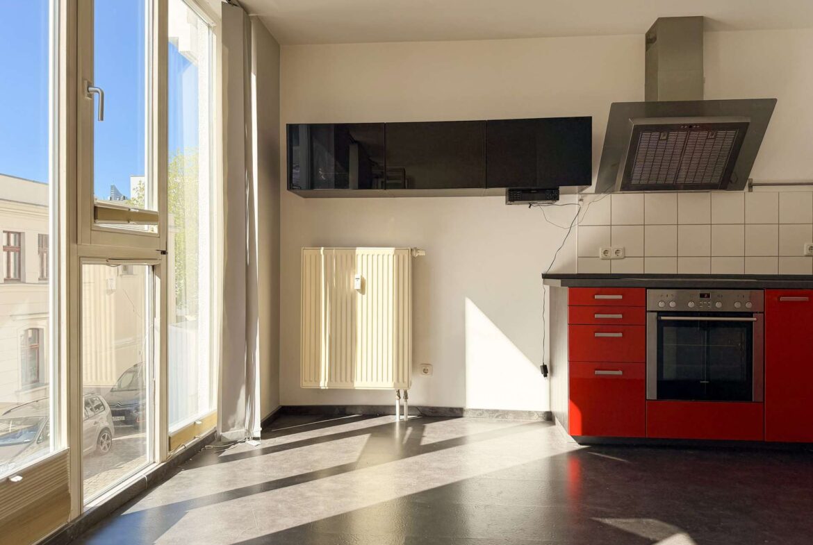 Bright kitchen corner with red lower cabinets, black wall units, and a stainless steel range hood under a vented chimney area.