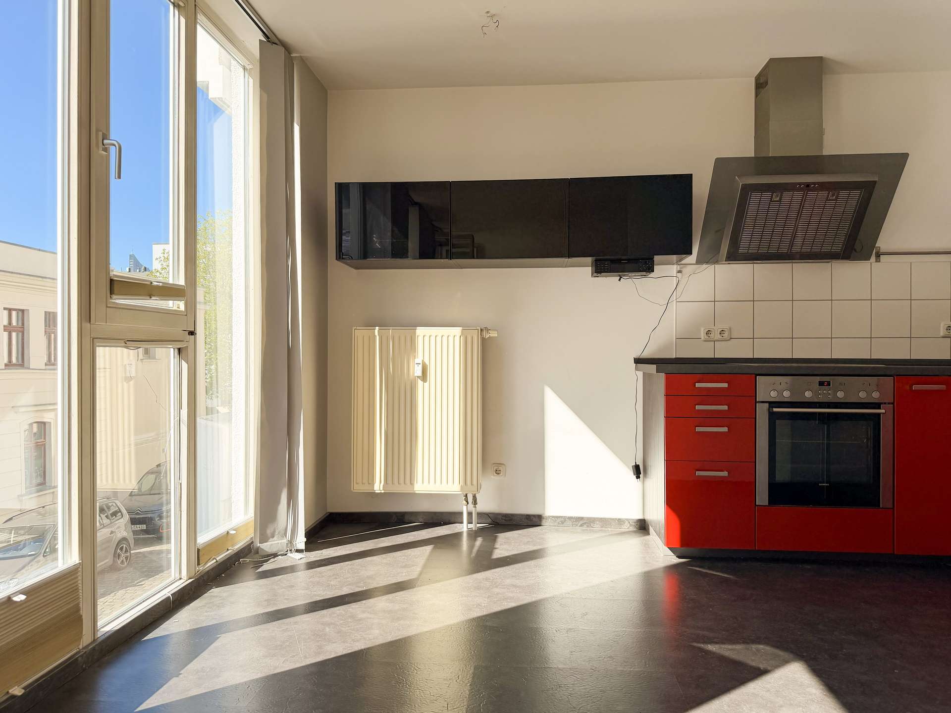 Bright kitchen corner with red lower cabinets, black wall units, and a stainless steel range hood under a vented chimney area.