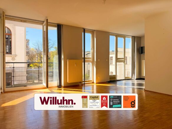 Sunlit empty living room with tall glass doors opening to a balcony and an advertising banner for Willuhn Immobilien at the bottom.