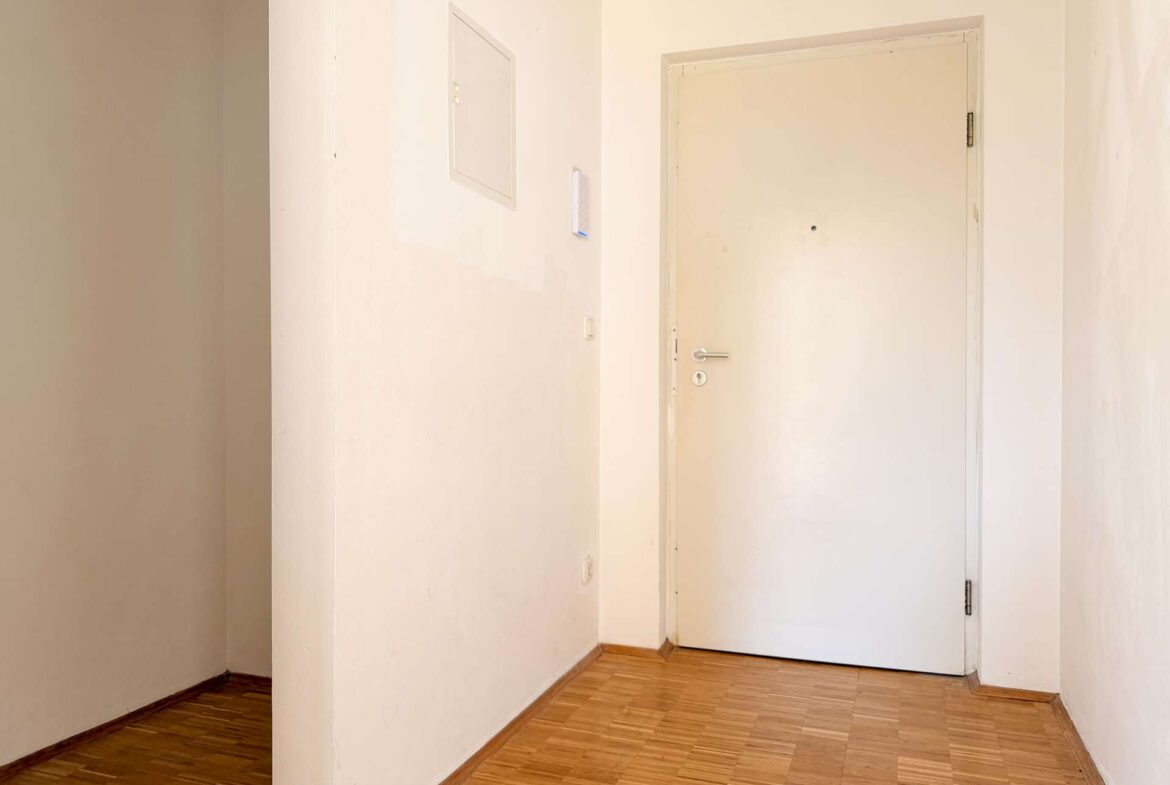 White hallway with a closed white door at the end and light wood flooring, beige walls, and minimal decor.
