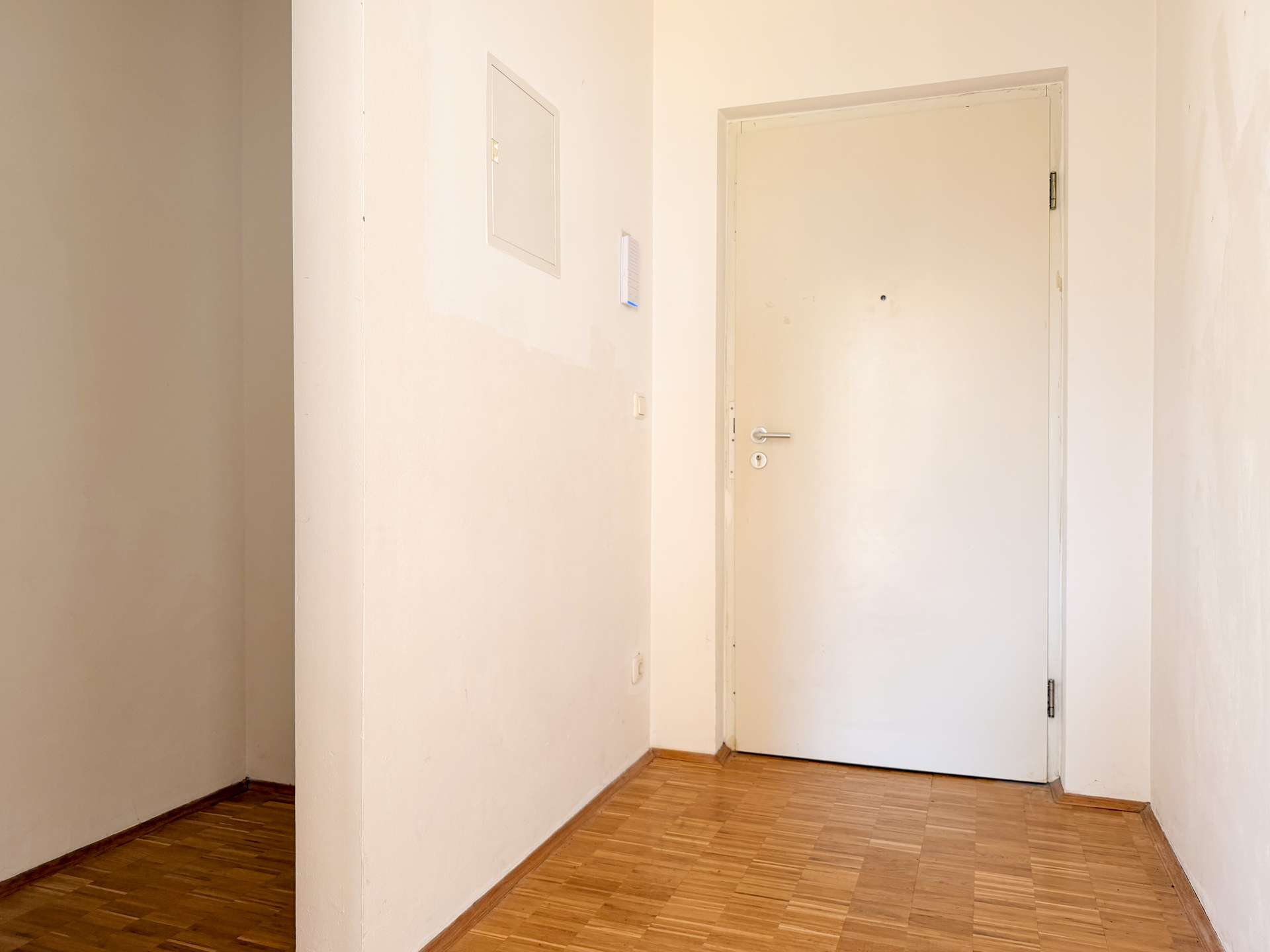 White hallway with a closed white door at the end and light wood flooring, beige walls, and minimal decor.