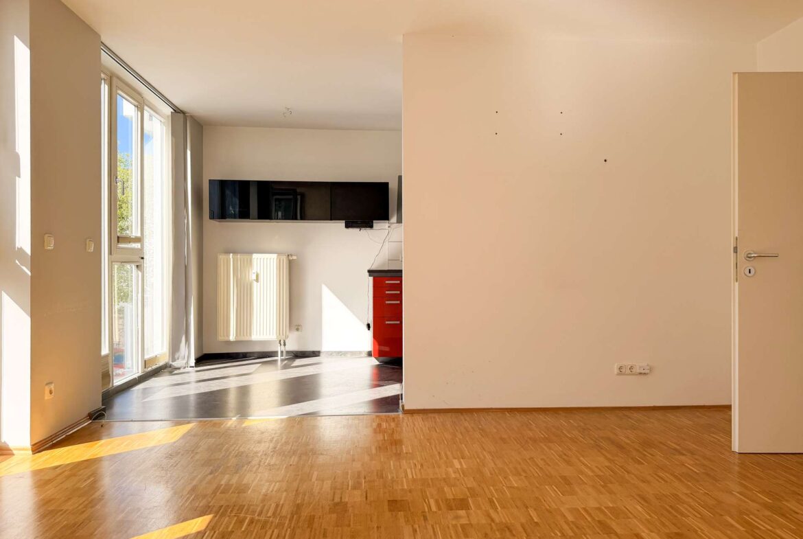 Sunlit interior with large left-side windows, a radiator, and a red tool cabinet against the back wall in an empty room.