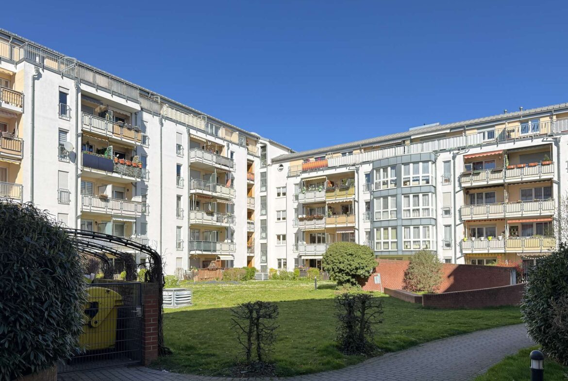 Residential apartment buildings surround a grassy courtyard under a clear blue sky.