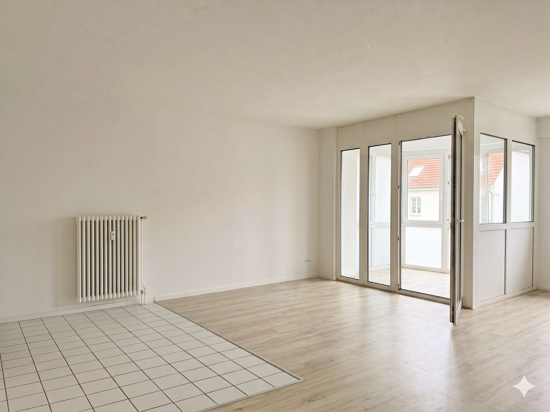 Bright, empty living area with white walls, a vertical radiator on the left, and large glass doors leading to an outside space; tiled floor transitions to wood.