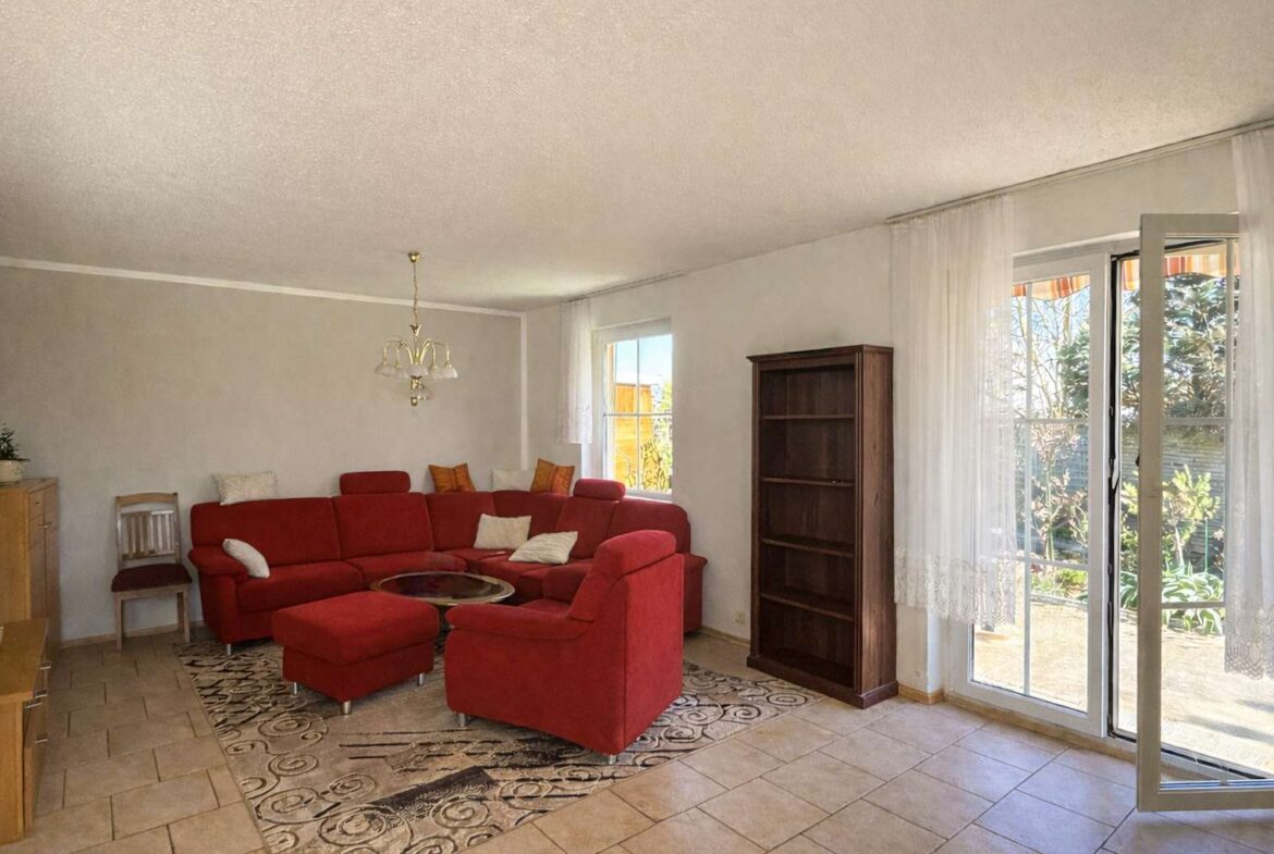 Living room with red sectional sofa, matching ottoman, and white cushions around a glass coffee table on a patterned rug.