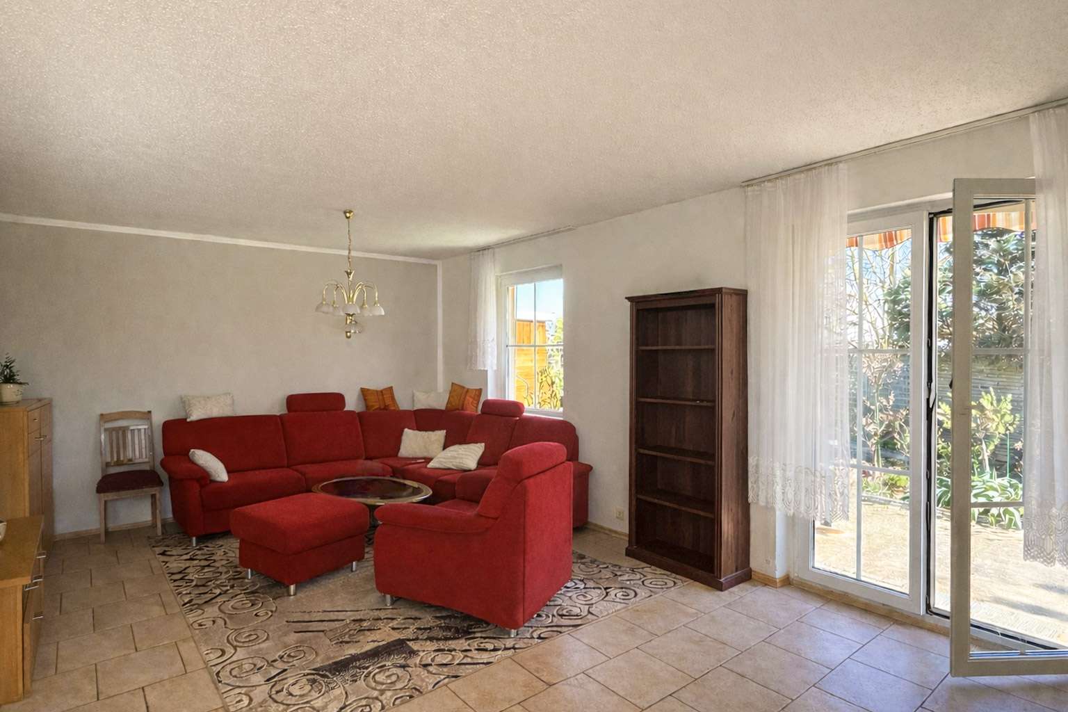 Living room with red sectional sofa, matching ottoman, and white cushions around a glass coffee table on a patterned rug.