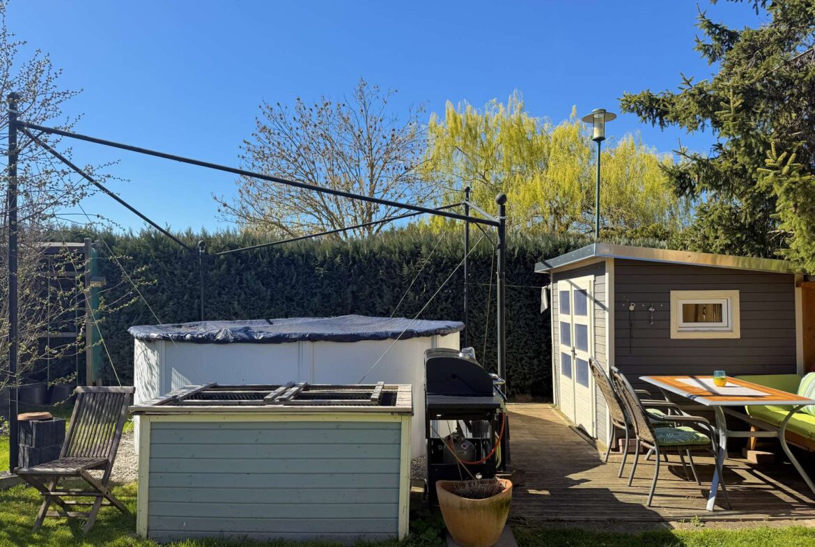 Backyard scene with a small shed, patio table and chairs, a covered pool, and potted plant under a clear blue sky.