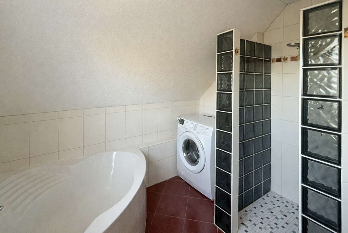 Bathroom corner with a front-loading washing machine next to a curved white bathtub and glass block partitions; red floor tiles.