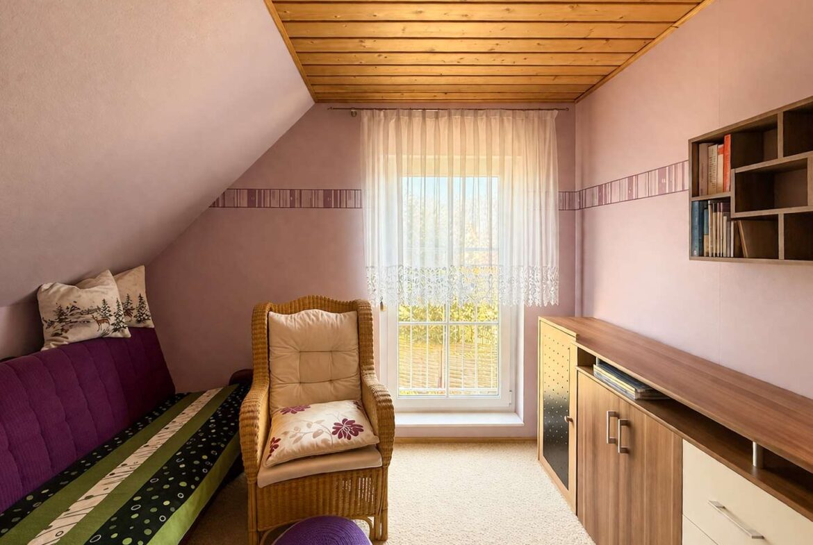 Cozy attic room with purple walls, wooden sloped ceiling, and a window with sheer lace curtains; wicker chair and purple sofa with cushions nearby.