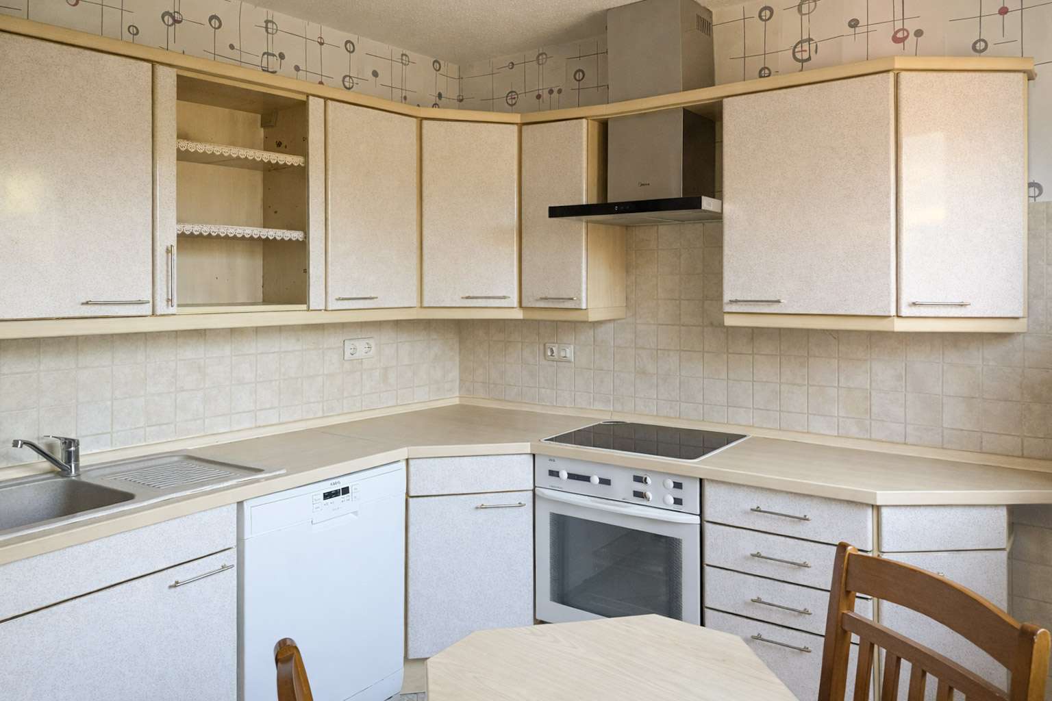 L-shaped kitchen with beige cabinets, tiled backsplash, range hood, built-in oven, electric stove, dishwasher, and a sink.