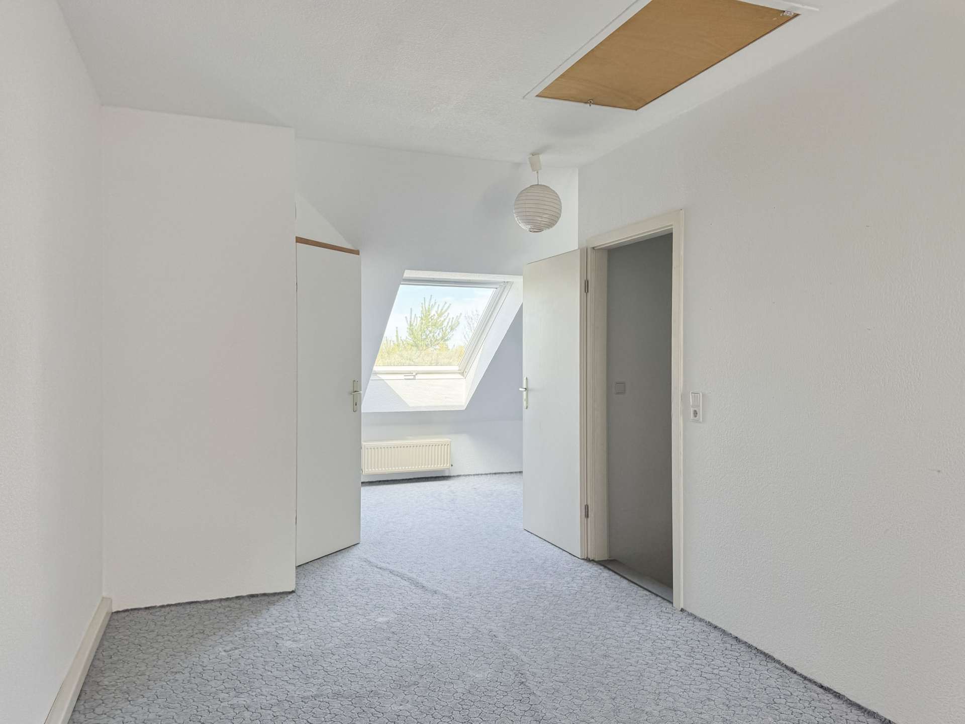 Bright white hallway with two open doors at the far end, a skylight and a hanging round paper lantern, pale patterned carpet.
