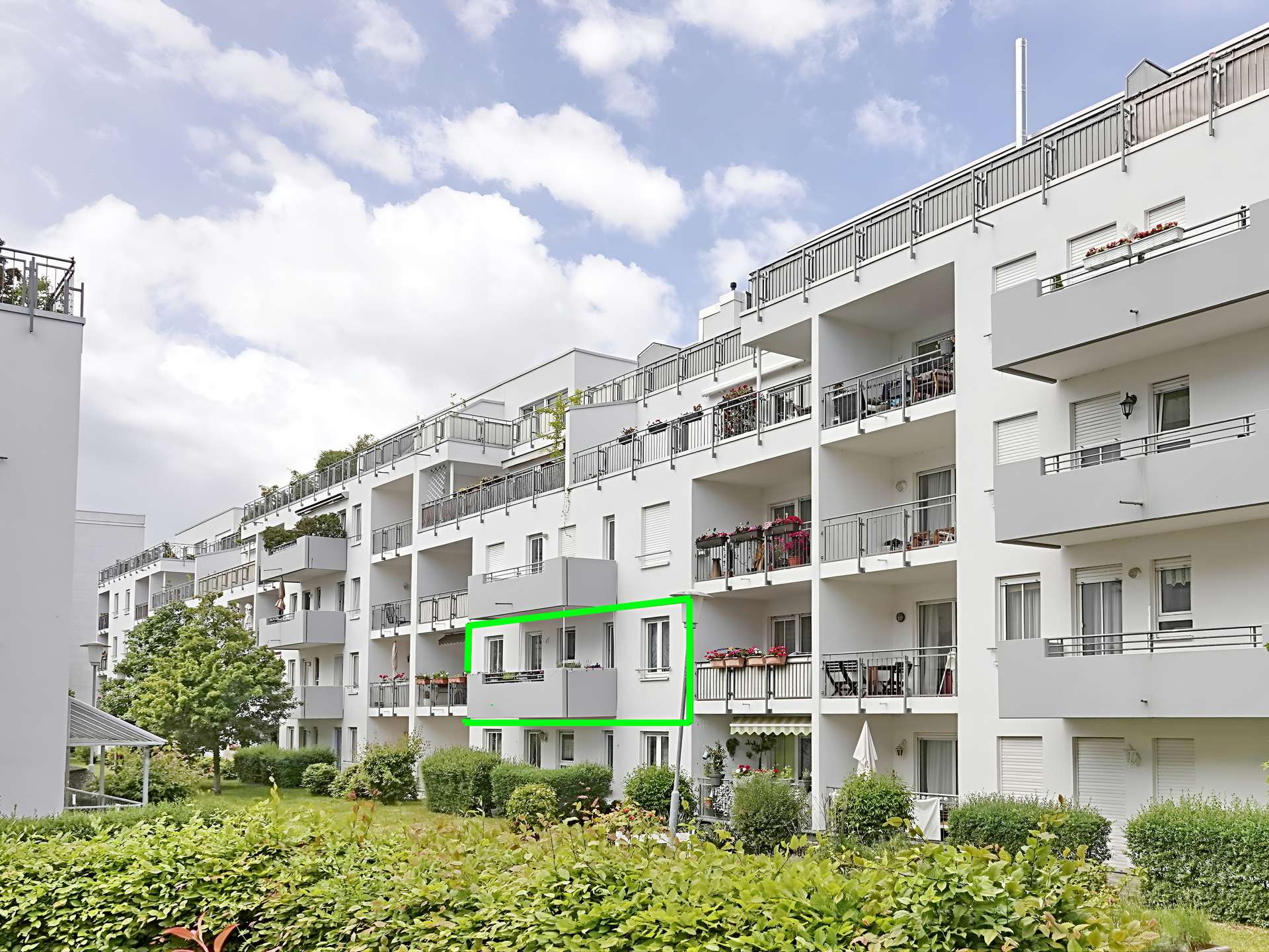 White apartment building with a balcony outlined in bright green on the second floor of the building edge.