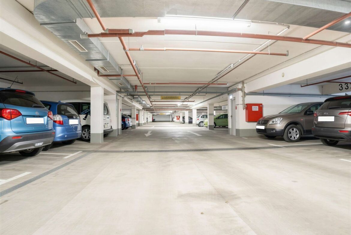 Underground parking garage with cars parked along both sides and a clear central driving lane in the distance.
