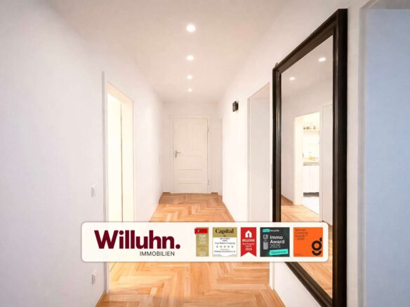Bright white hallway with a herringbone wooden floor, end door, and a large dark-framed mirror on the right; branding and award badges across the bottom.