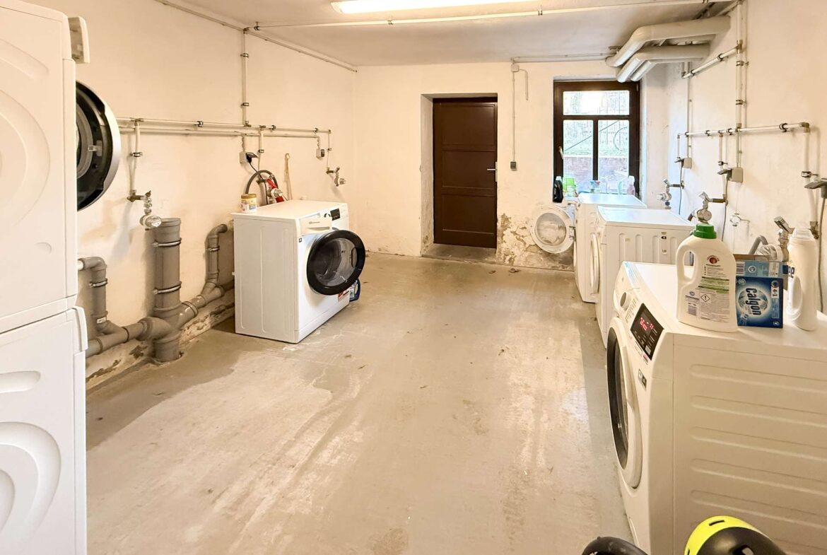 Basement laundry room with front-loading washer and dryer amid exposed pipes and a concrete floor.