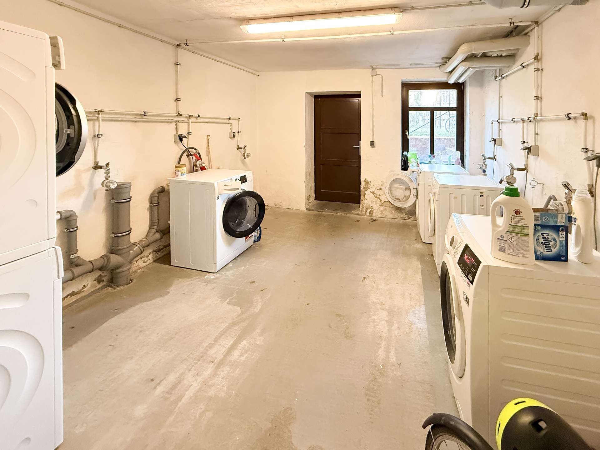 Basement laundry room with front-loading washer and dryer amid exposed pipes and a concrete floor.