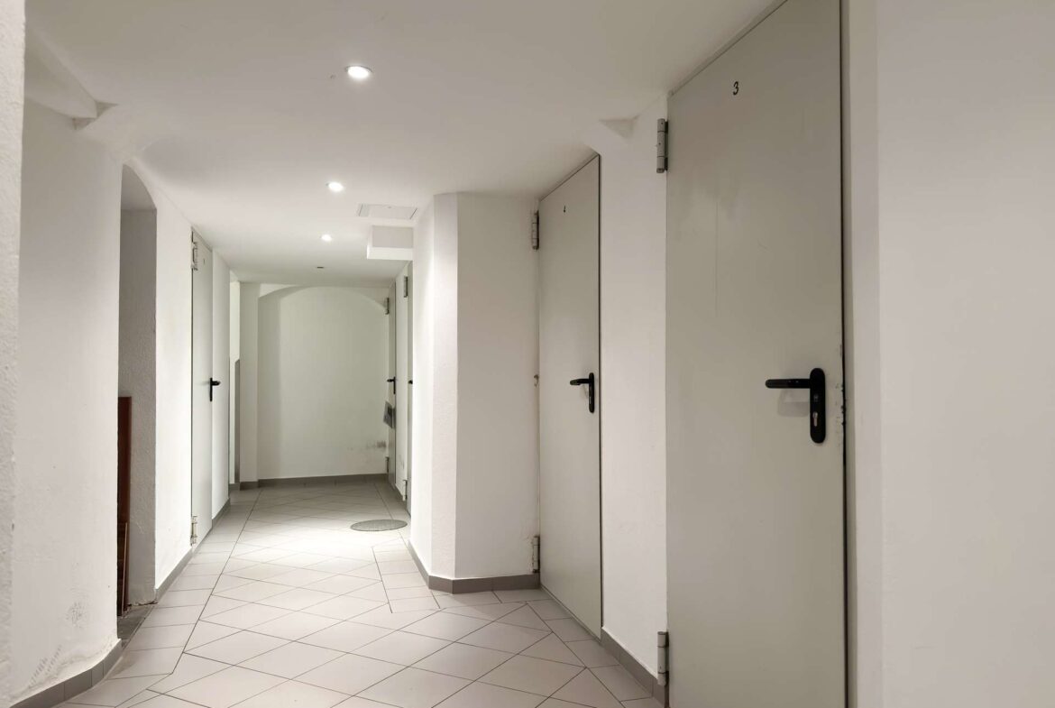 White, well-lit corridor with numbered gray doors along the right side and a tiled floor in a residential-looking building.