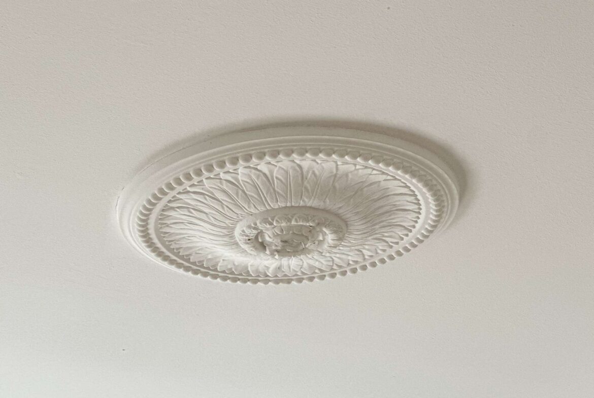 White decorative ceiling light fixture with an ornate circular medallion mounted to a beige ceiling