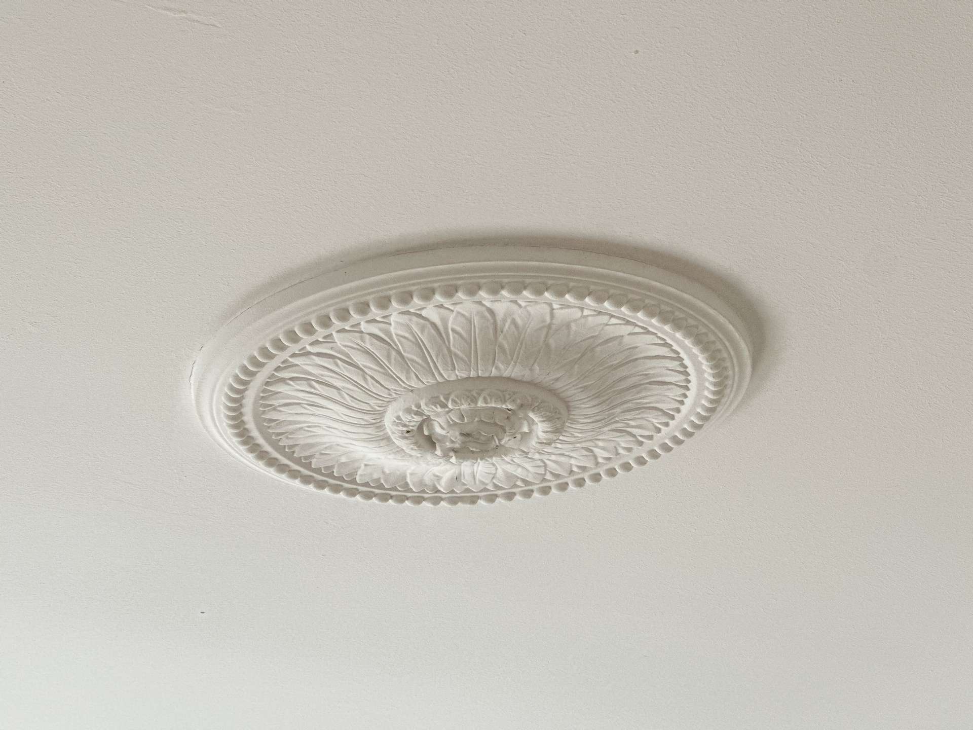 White decorative ceiling light fixture with an ornate circular medallion mounted to a beige ceiling