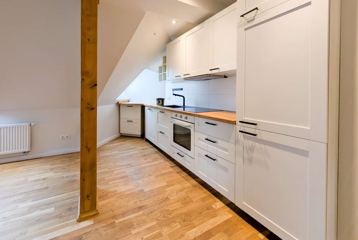 Bright white kitchen with wood countertop, built-in oven, and slanted ceiling, exposed wooden beam in foreground.