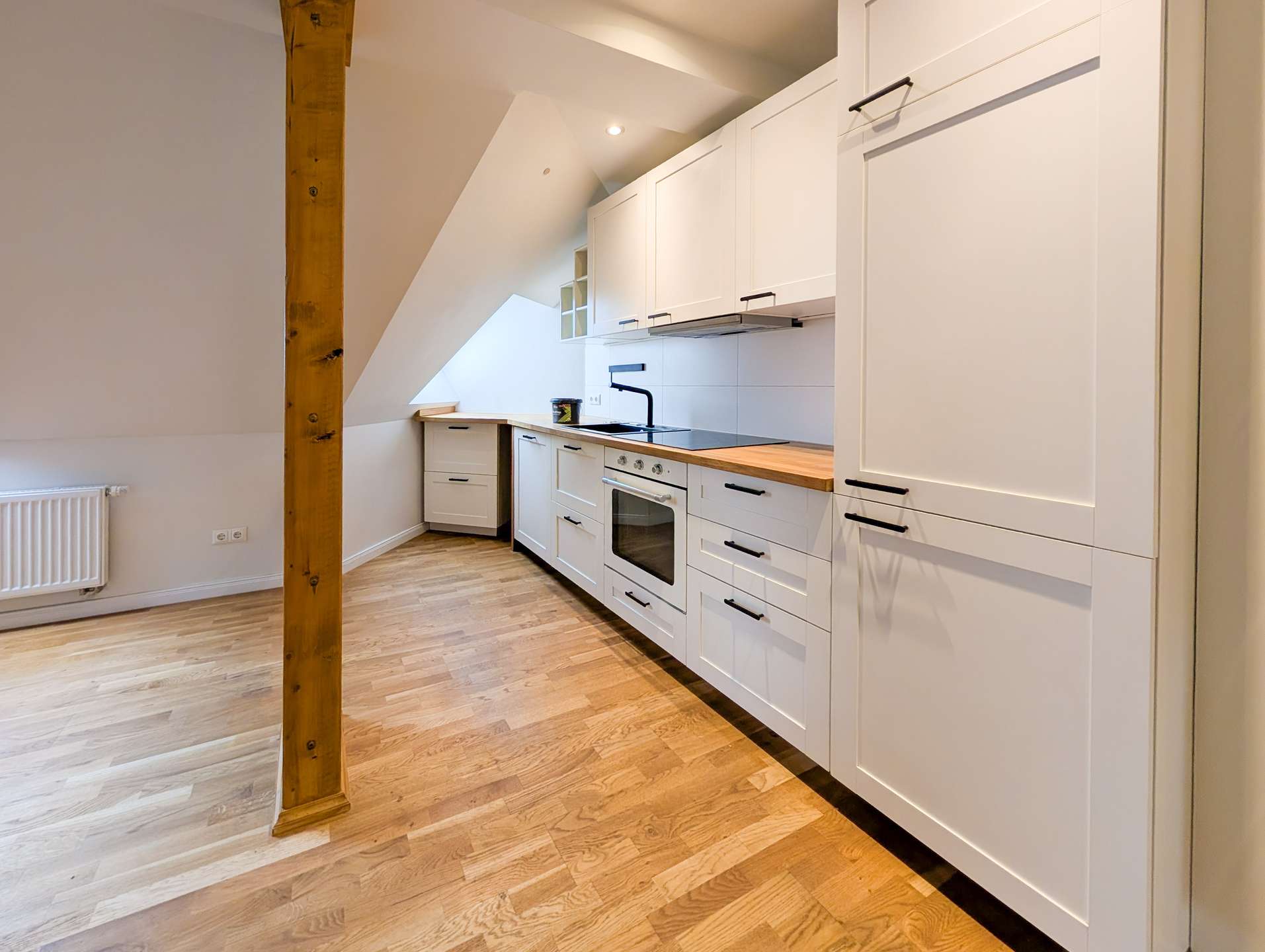 Bright white kitchen with wood countertop, built-in oven, and slanted ceiling, exposed wooden beam in foreground.