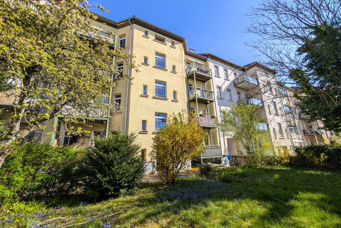 Residential apartment building with balconies surrounded by trees and a clear blue sky
