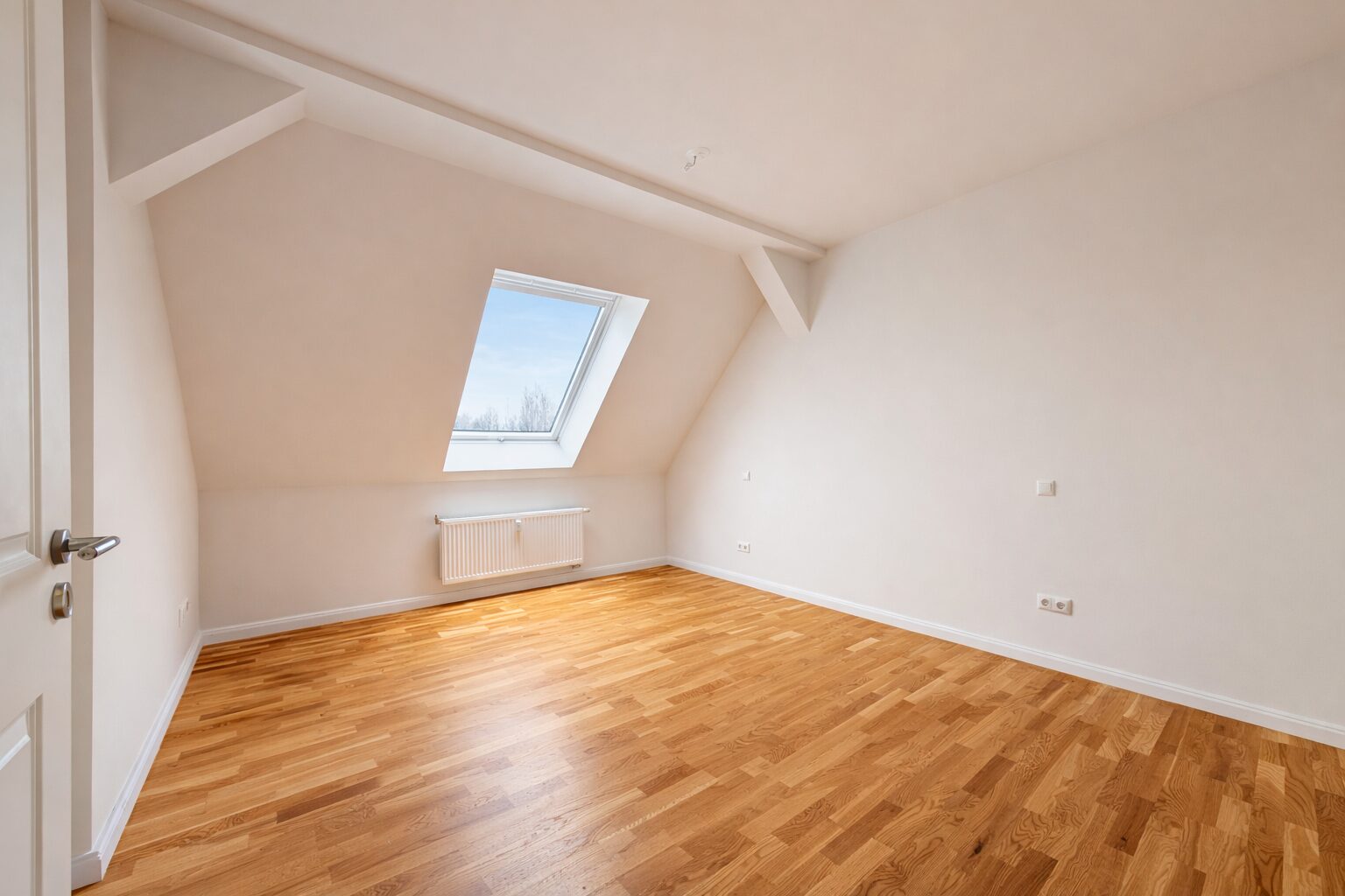 Spacious empty attic room with a sloped ceiling, a skylight window, and a radiator under the window, wood floor.