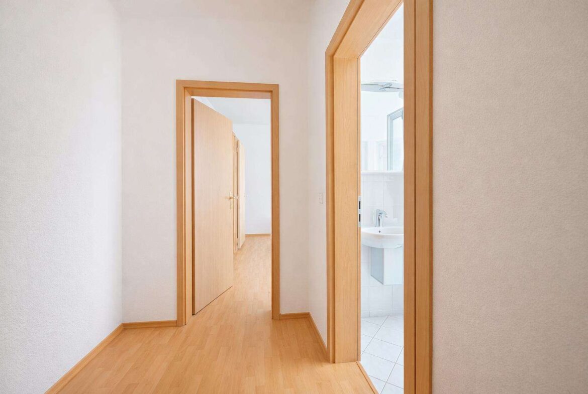 Hallway with light wood flooring and open wooden door frames; a bathroom is visible on the right.
