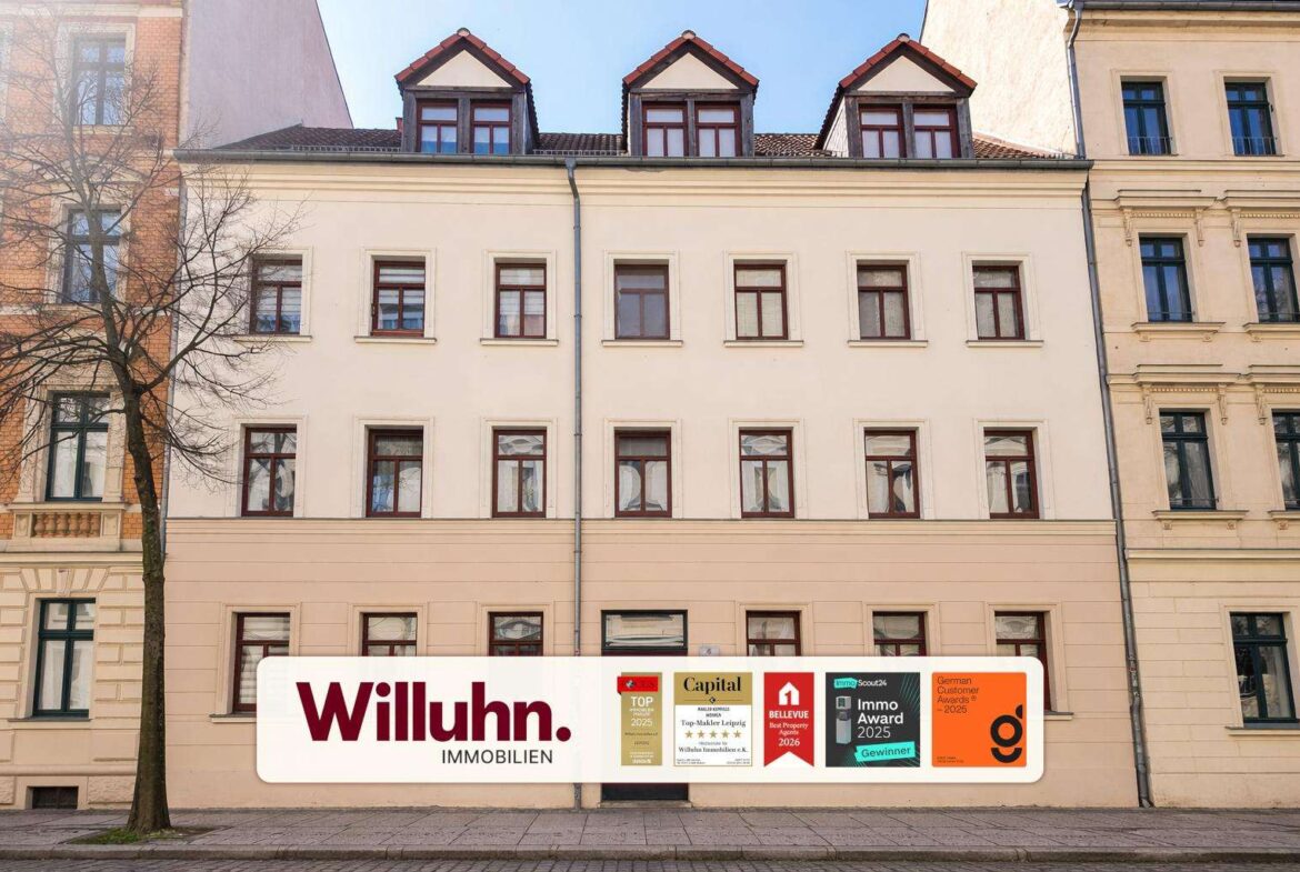 White real estate banner on a beige building that reads 'Willuhn. Immobilien' with multiple award plaques along the bottom edge, at street level.