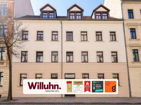White real estate banner on a beige building that reads 'Willuhn. Immobilien' with multiple award plaques along the bottom edge, at street level.