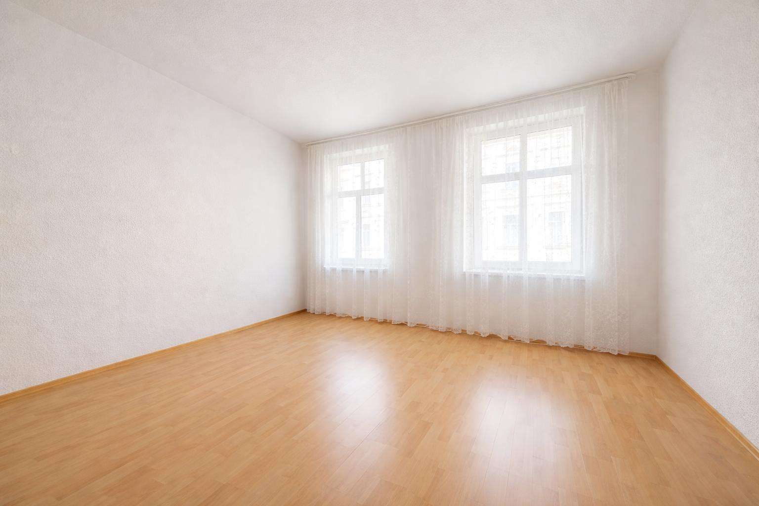Empty bright room with light wooden floor and white walls, large windows with sheer curtains