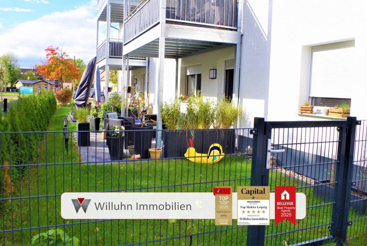 Exposed fenced courtyard of a modern apartment building with outdoor seating, potted plants, and yellow pool float near the gate, signs for a real estate agency visible on the fence