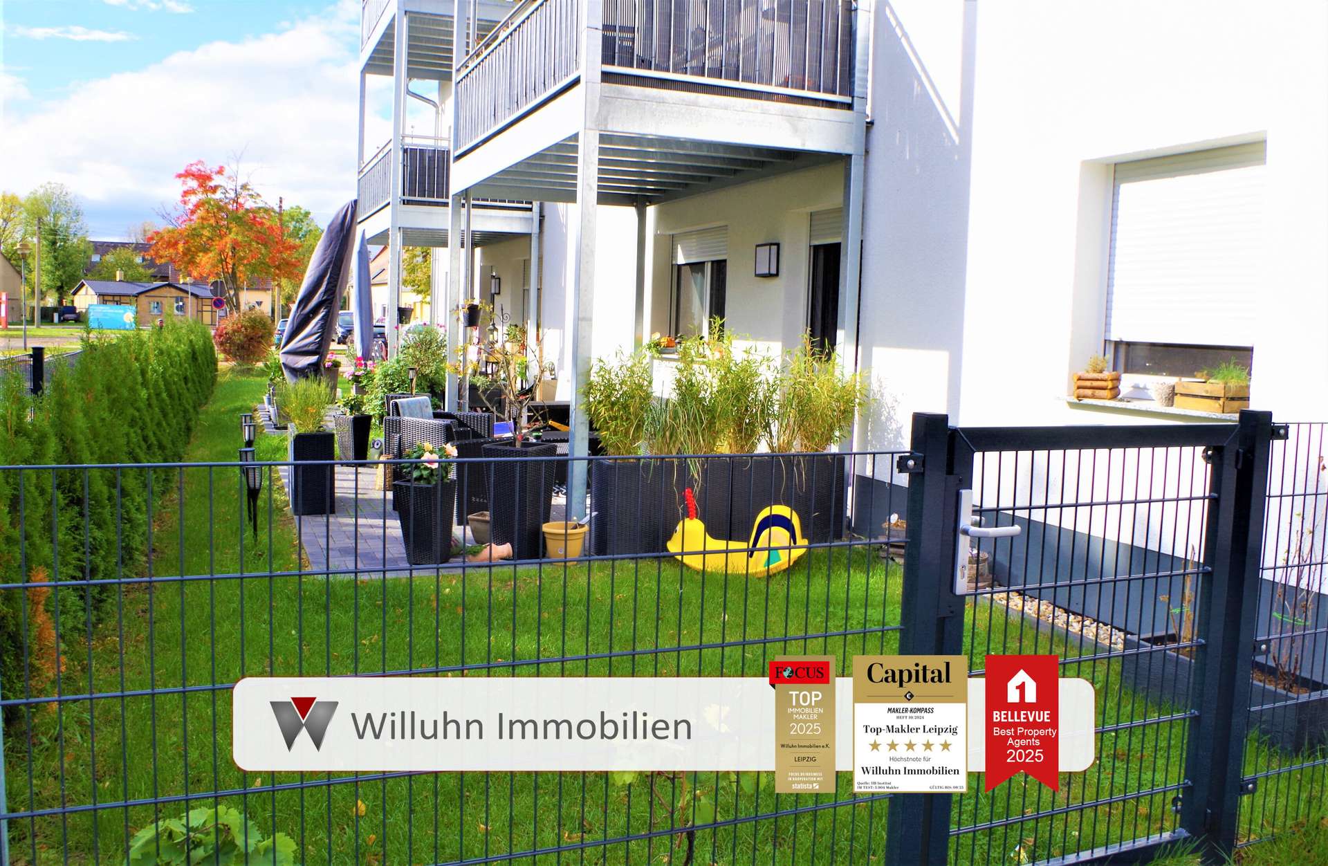 Exposed fenced courtyard of a modern apartment building with outdoor seating, potted plants, and yellow pool float near the gate, signs for a real estate agency visible on the fence