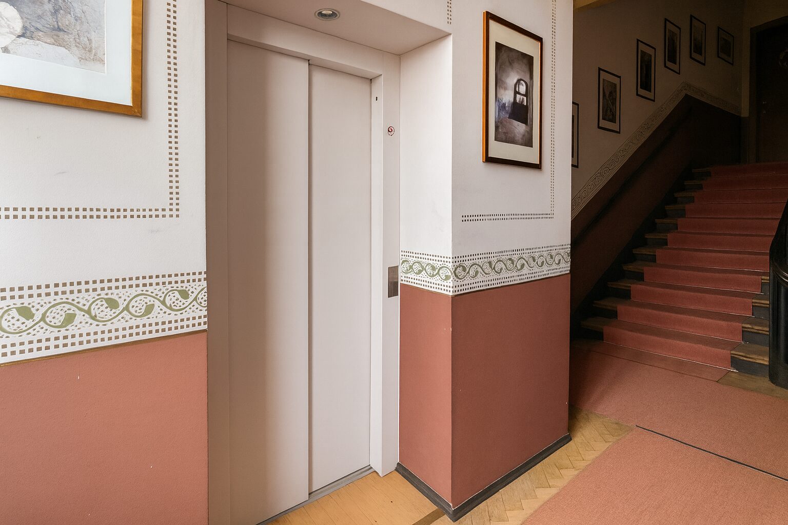 Elevator doors in a decorative hallway with framed art and a staircase to the right.