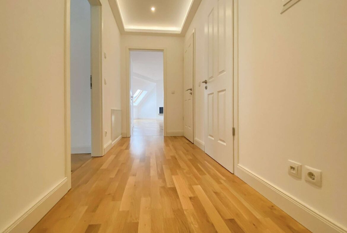Bright white hallway with light wood flooring and white doors, leading to a sunlit room.