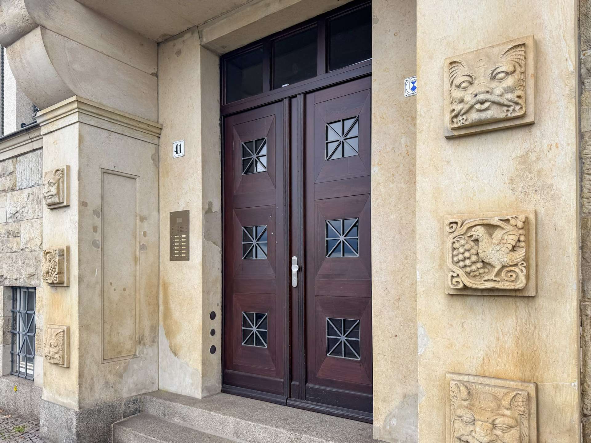 Beige stone building entry with dark wooden double doors and decorative square-window panes; house number 41 on the wall.