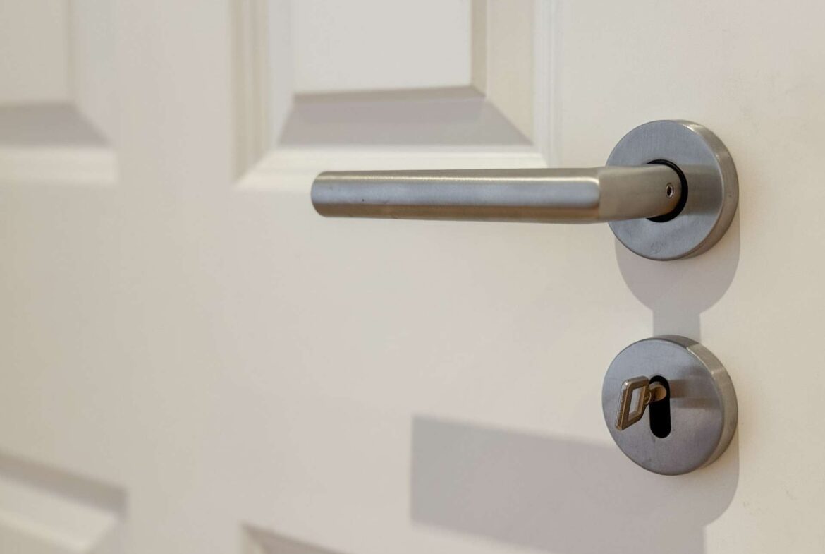Close-up of a silver door lever with a round escutcheon and a key inserted in the bottom lock