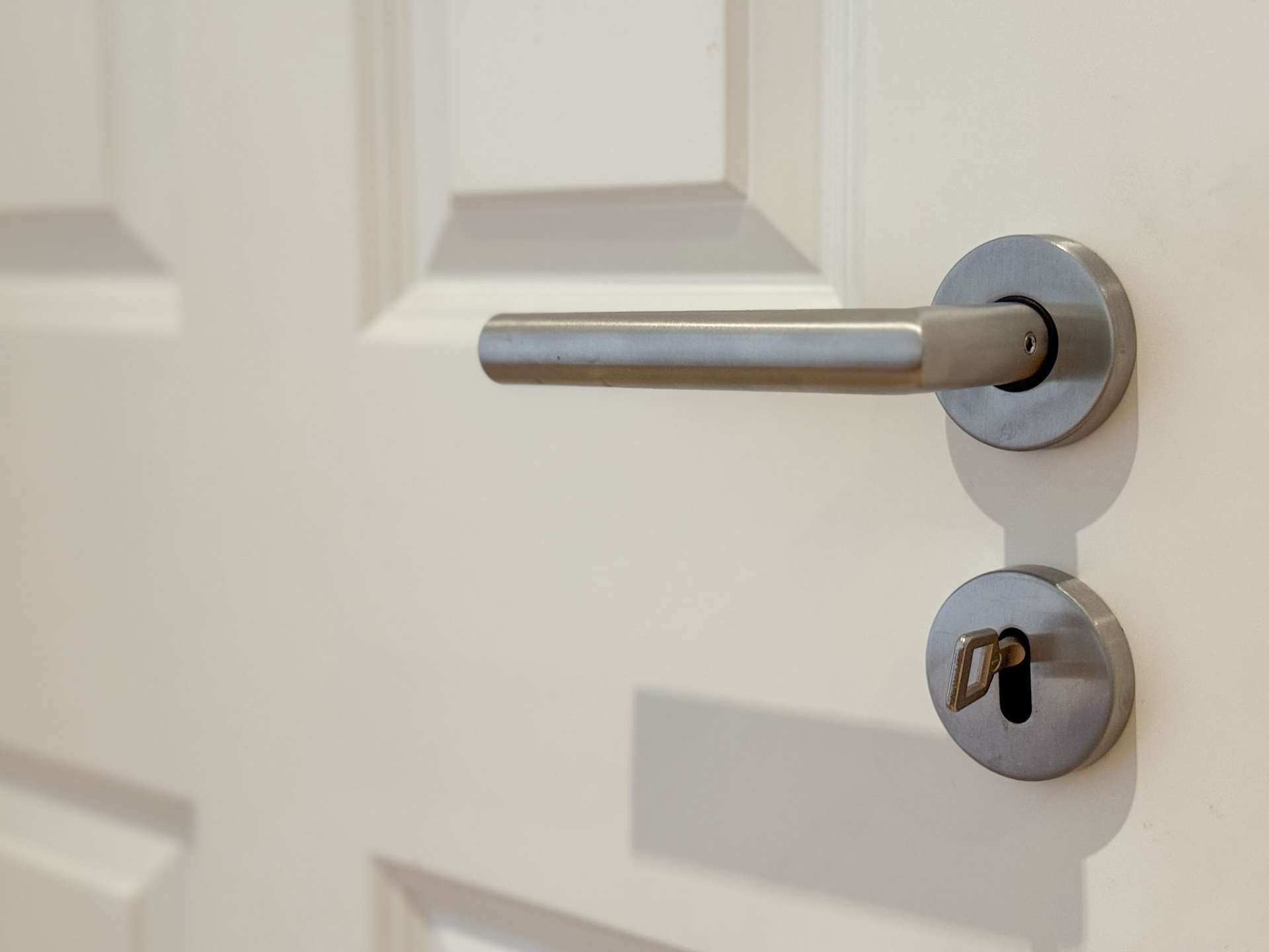 Close-up of a silver door lever with a round escutcheon and a key inserted in the bottom lock
