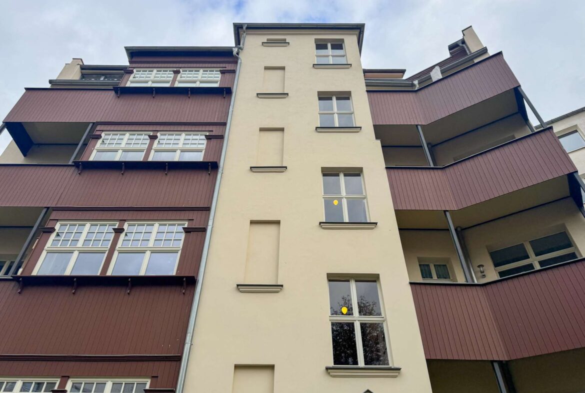 Low-angle view of a multi-story residence with a beige central tower and burgundy balconies on both sides.