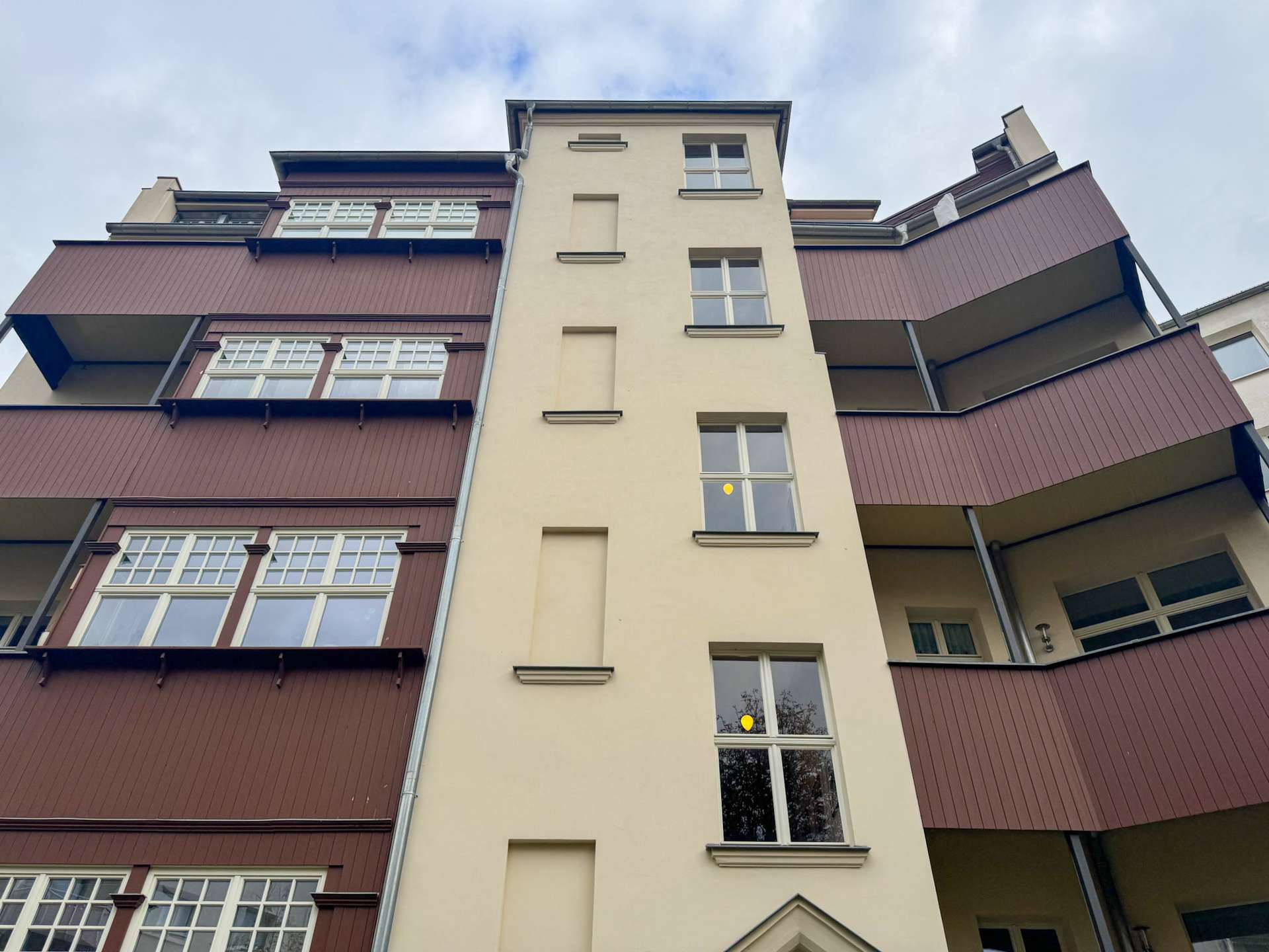 Low-angle view of a multi-story residence with a beige central tower and burgundy balconies on both sides.