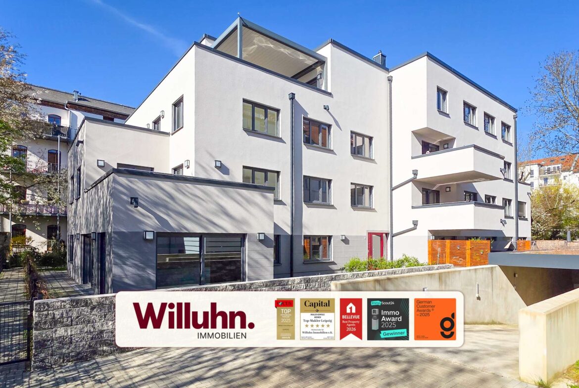 White modern apartment building with several windows and balconies under a clear blue sky; Willuhn Immobilien sign in the foreground.