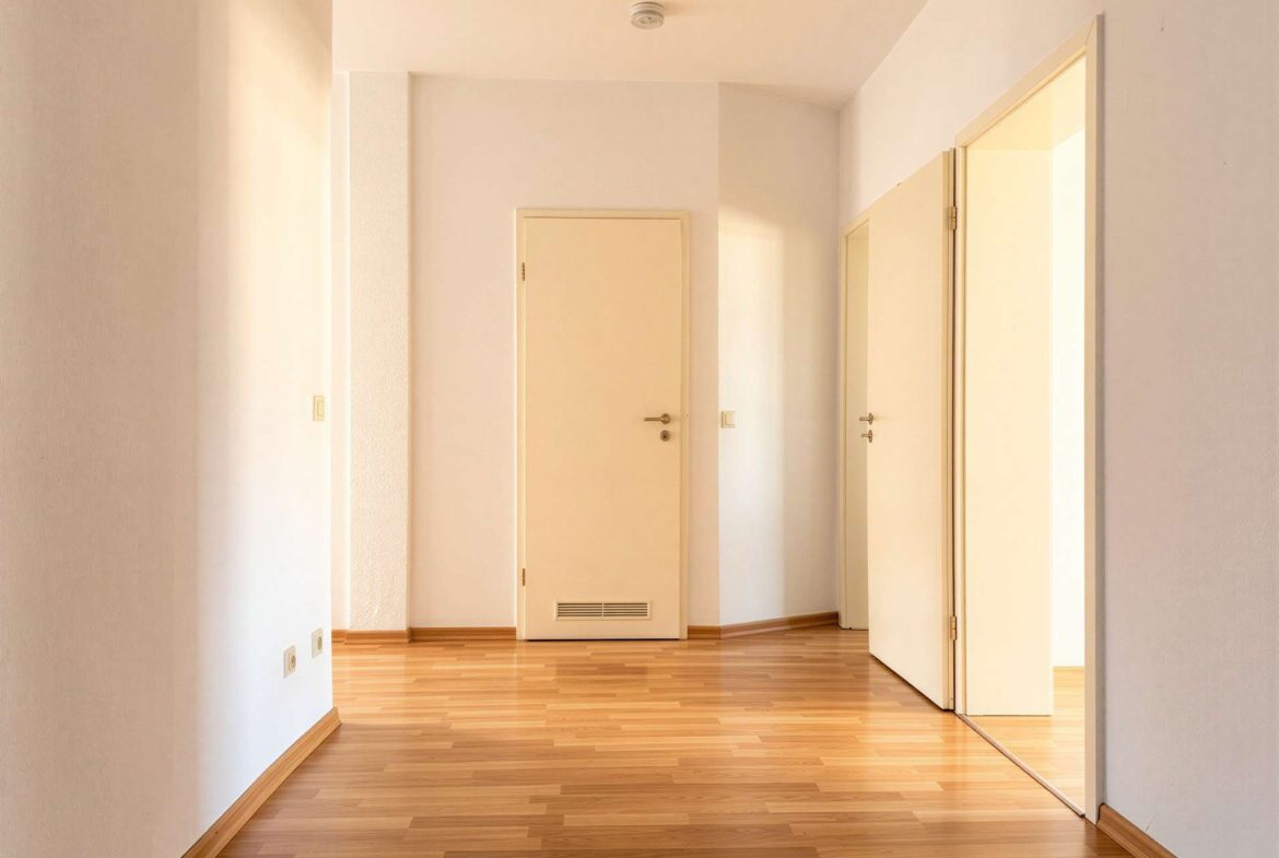 Bright hallway in a residential interior with white walls and several closed doors along a corner, wooden floor.