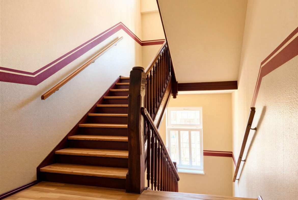 Wood staircase with dark railing, beige walls, and purple decorative trim; windows at the bottom letting in light.