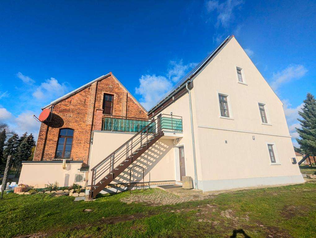 Two-tone building with a brick left section and white right section, connected by an external metal staircase under a blue sky.