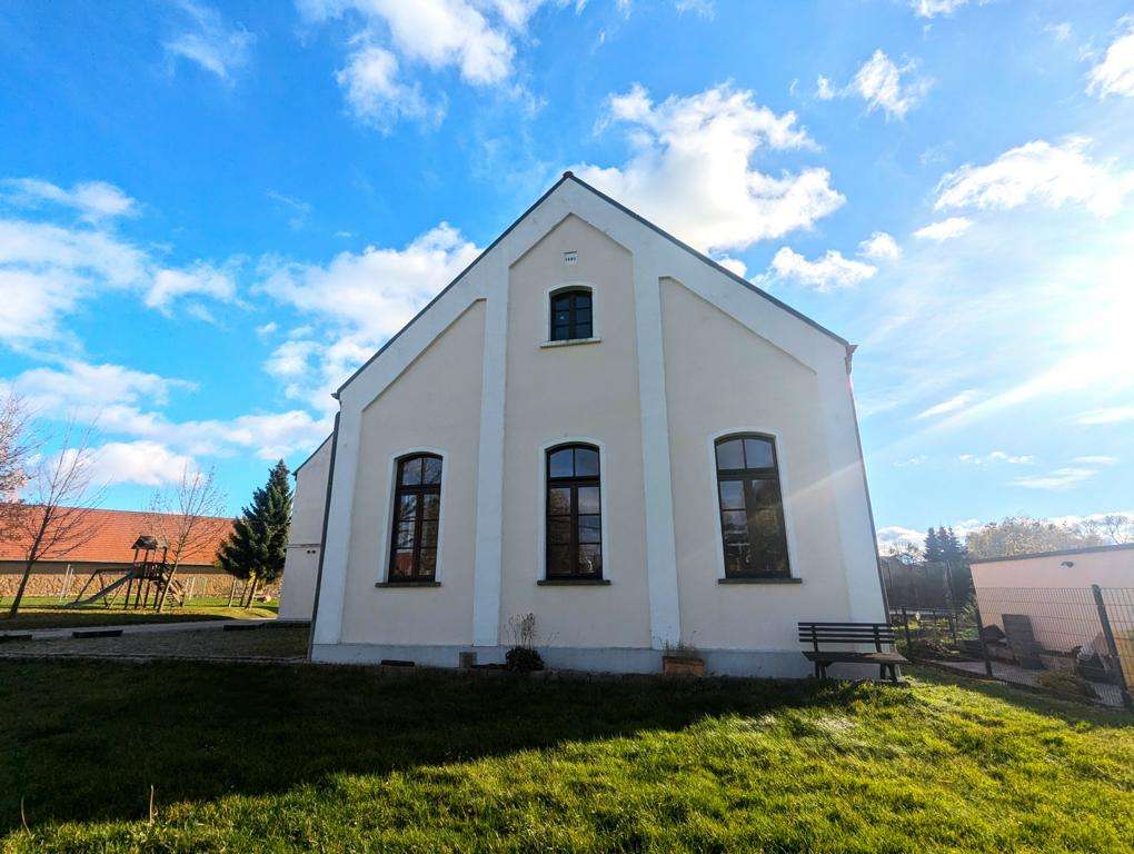 Front view of a small white church with three tall arched windows on a sunny day, a grassy yard in the foreground.