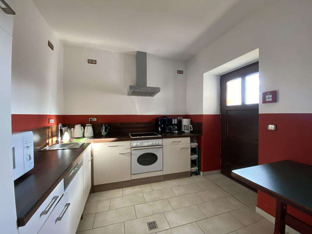 Kitchen with white cabinets, red backsplash, stove and oven with range hood, and a dark table by the door on the right.