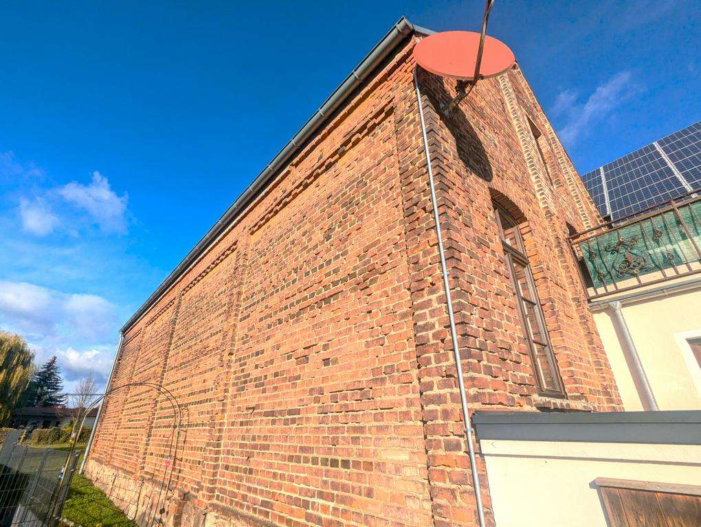 Brick building corner with a red satellite dish on the roof and solar panels on a neighboring roof against a blue sky.