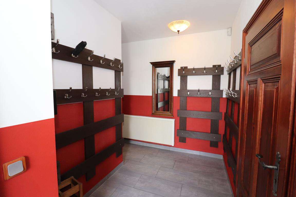 Coat racks with many hooks lining red-and-white walls in a narrow hallway, with a wooden door on the right and a mirror ahead
