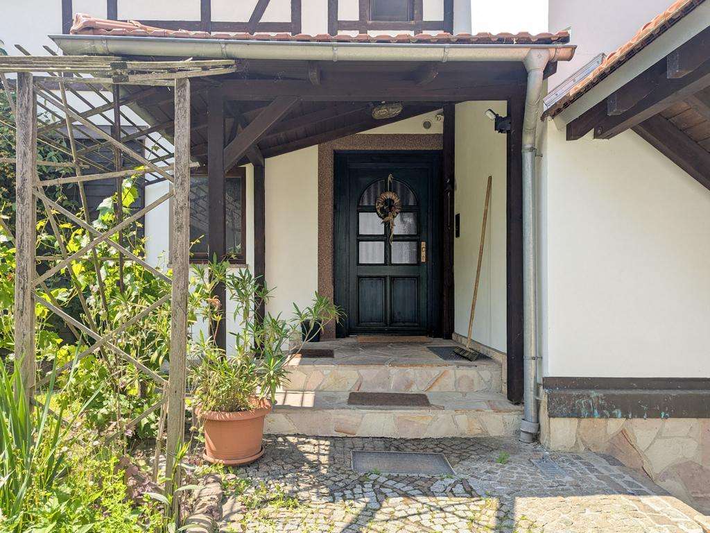 Front entry with a dark door and wreath, stone steps, and potted plants on a stone walkway under a covered porch of a house.