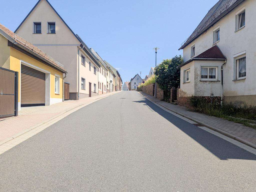 Sunlit residential street lined with houses on both sides and a clear blue sky